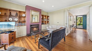 A spacious living room with a fireplace, wooden shelves, a comfortable sofa, and a television. - Blue Mountains Rhapsody - Point Blank Views Clifftop (Leura)