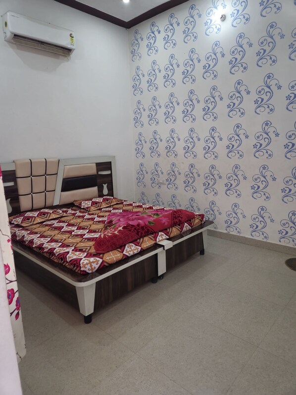 A bedroom with a bed, a headboard, a wall air conditioner, and patterned wallpaper. - Shyam Niwas Guest House (Danta Ramgarh)