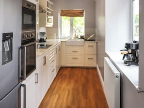 Cozinha moderna com eletrodomésticos de aço inoxidável, armários brancos e piso de madeira.