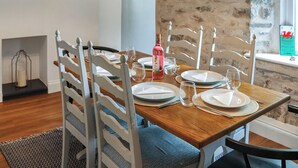 Comedor con mesa de madera dispuesta para cuatro, sillas blancas y un reloj de pared verde.