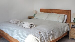 Una cama bien tendida con ropa de cama a rayas y dos almohadas, un cabecero de madera y una mesita de noche con una lámpara.