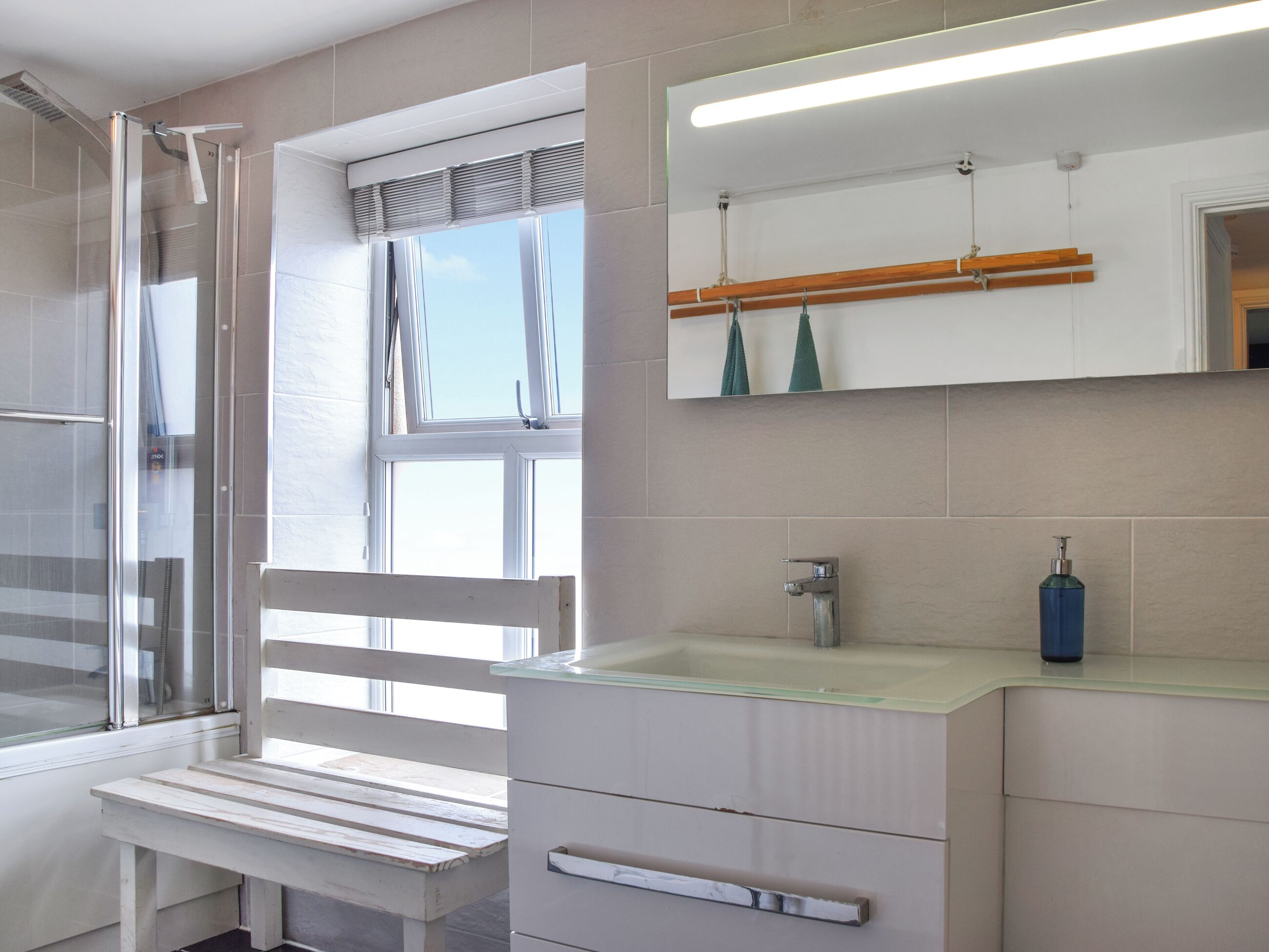 Une salle de bain avec une douche, un banc, un lavabo et un miroir.