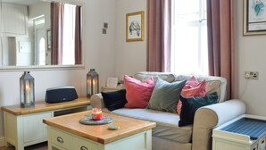 Ein gemütliches Zimmer mit einer Couch, einem kleinen Tisch mit Kerze, einem Spiegel und einem Fenster mit Vorhängen.