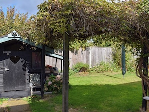 A wooden shed with a heart-shaped cutout, a small porch, and a garden area with grass and plants. - 2 bedroom accommodation in Pakefield, near Lowestoft (Pakefield, near Lowestoft)