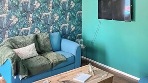 A room with a blue sofa, a wooden coffee table, and a wall-mounted TV. - 2 bedroom accommodation in Pakefield, near Lowestoft (Pakefield, near Lowestoft)