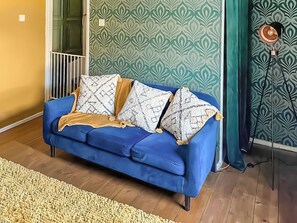 Un sofá azul con cojines estampados, suelo de madera y papel tapiz decorado.