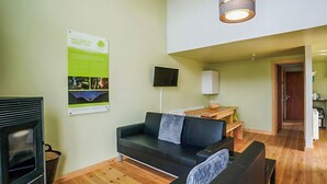A modern living room with a black sofa, wooden flooring, a fireplace, and a dining area with a table and chairs. - Modern comfort meets rugged wilderness at Tarset Tor’s unique glamping retreat. (Hexham, near Bellingham)