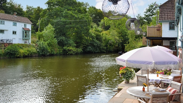 A riverside patio with outdoor seating, a dining table, and a hanging light fixture. - 1 bedroom accommodation in Ruswarp, near Whitby (Ruswarp, near Whitby)