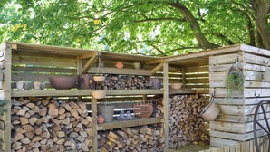 A rustic wooden structure with shelves for storage, a wheelbarrow, and a hanging plant.
