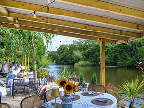 An outdoor dining area with tables set for two, surrounded by lush greenery and a river view. - Honeysuckle - UK50453 (Ruswarp, near Whitby)