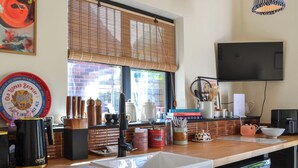 A kitchen with a wooden countertop, a white sink, a black coffee machine, and a window with bamboo blinds.
