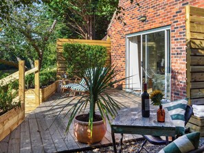 Een houten terras met een tafel, stoelen, een bloempot en een fles wijn.