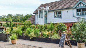 A traditional building with a tiled roof, a front porch, and a garden with various plants.