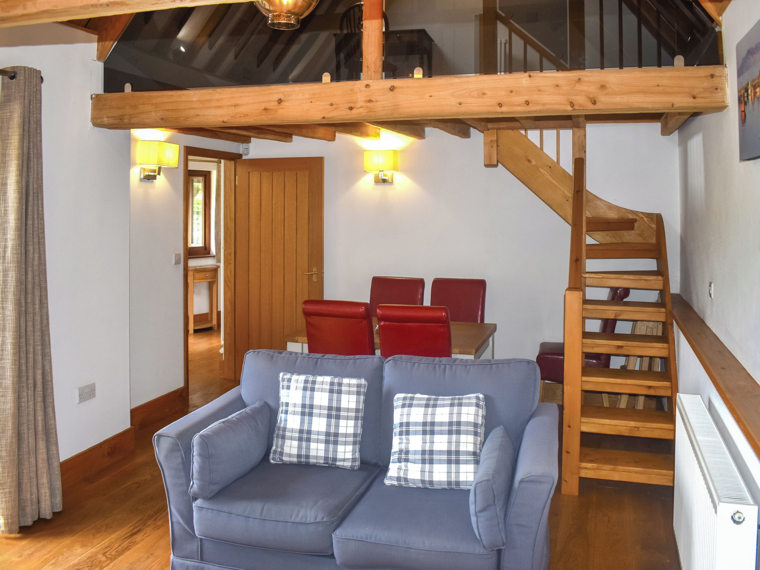 A cozy living room with a blue sofa, red chairs, a wooden staircase, and a dining area with a table and chairs.