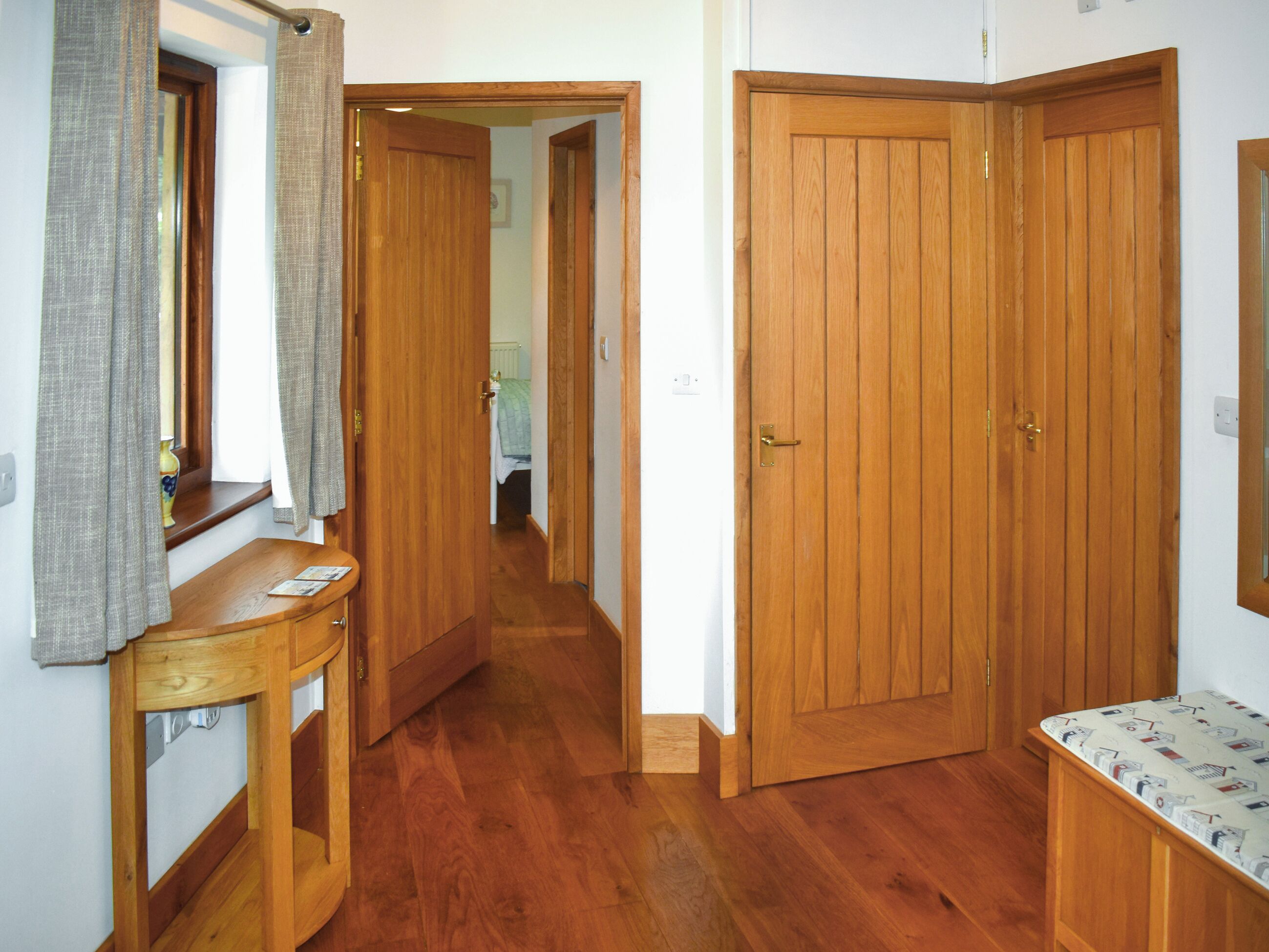 A hallway with wooden flooring, a wooden door, and a small table with a mirror.
