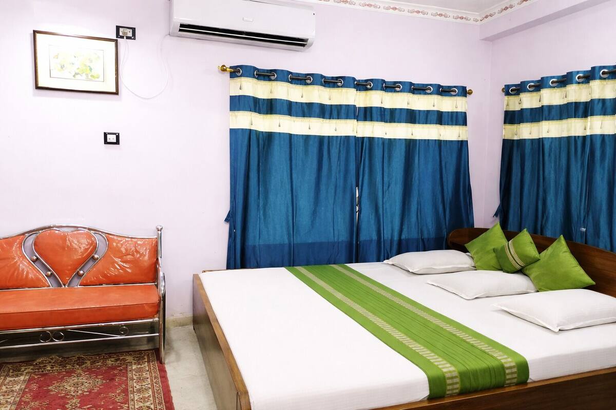 A bedroom with a bed, a sofa, curtains, and an air conditioning unit.