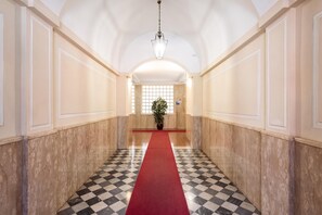 A hallway with a checkered floor, a red carpet, and a chandelier.