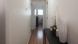 A hallway with a wooden floor, white walls, and a black table with decorative items.