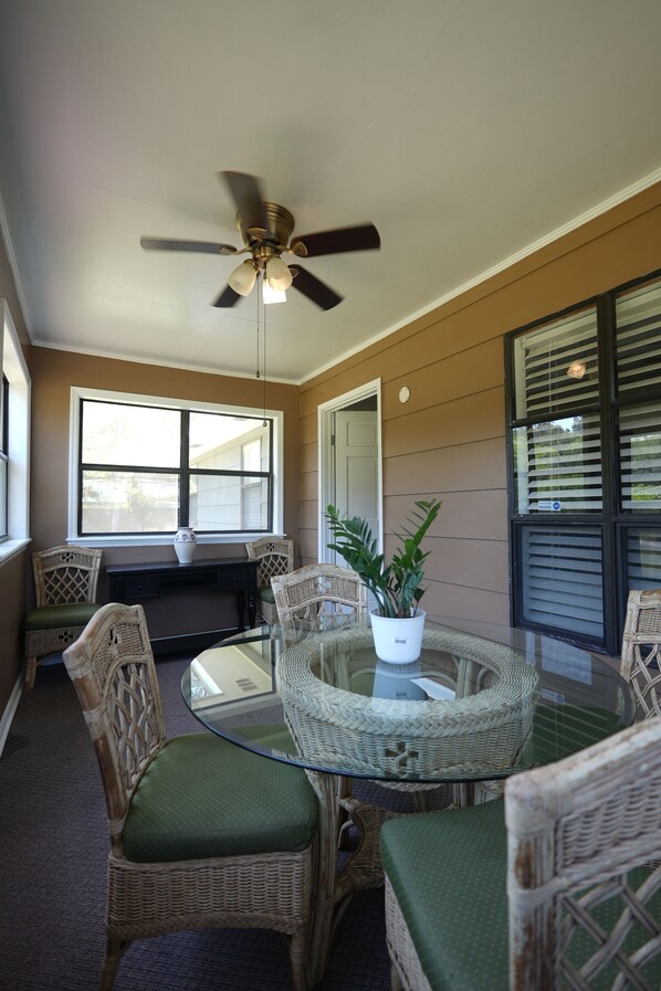 A dining area with wicker chairs, a glass table, and a ceiling fan.