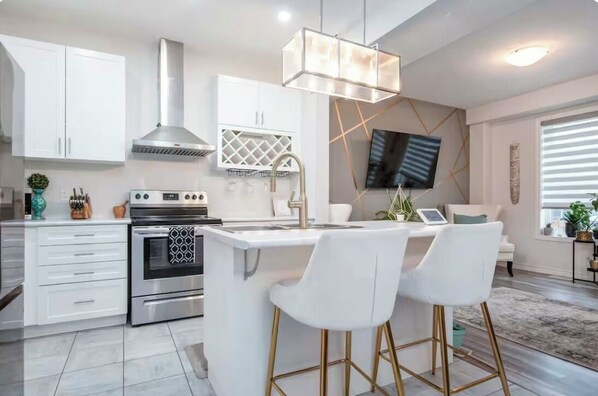 A modern kitchen with white cabinetry, a stainless steel range, and a bar area with white bar stools. - Comfy 3bed Woodstock Escape Upper Level home with 2nd floor Living Room,AC +more (Woodstock)