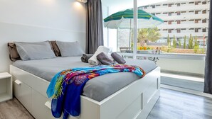 Una habitació d'hotel moderna amb un llit gran, vistes a la ciutat i un balcó amb taula i cadires.