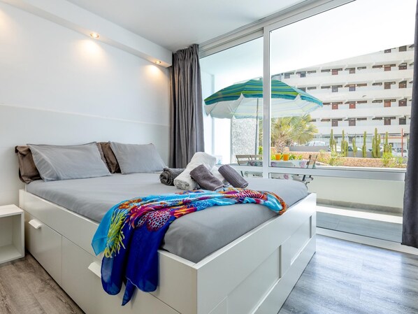 Une chambre d’hôtel moderne dotée d’un grand lit, offrant une vue sur le paysage urbain et comprenant un balcon avec une table et des chaises.