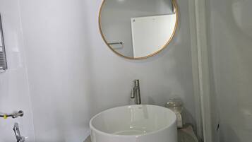 Un baño con espejo redondo, lavabo blanco y ducha de mano.