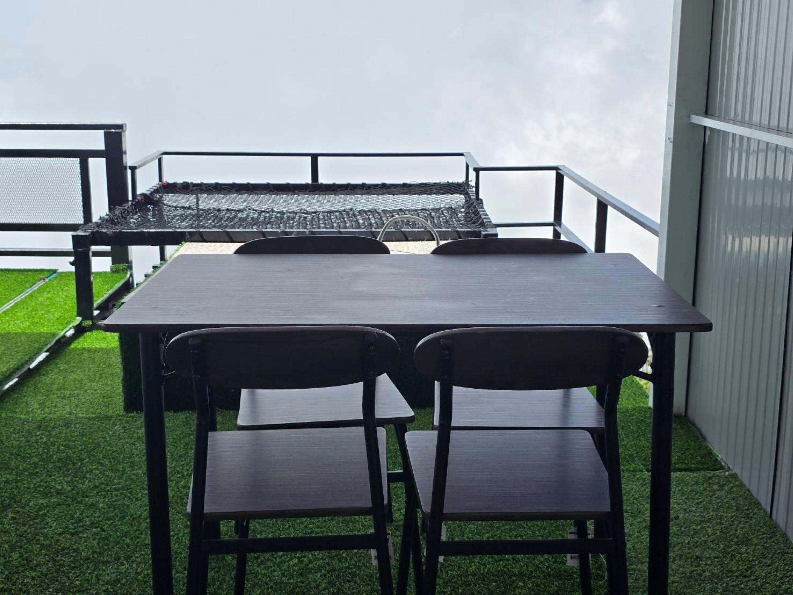 Um pátio externo com mesa e cadeiras, cercado por um corrimão de metal e vista do céu.