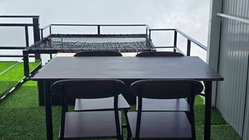 Um pátio externo com mesa e cadeiras, cercado por um corrimão de metal e vista do céu.