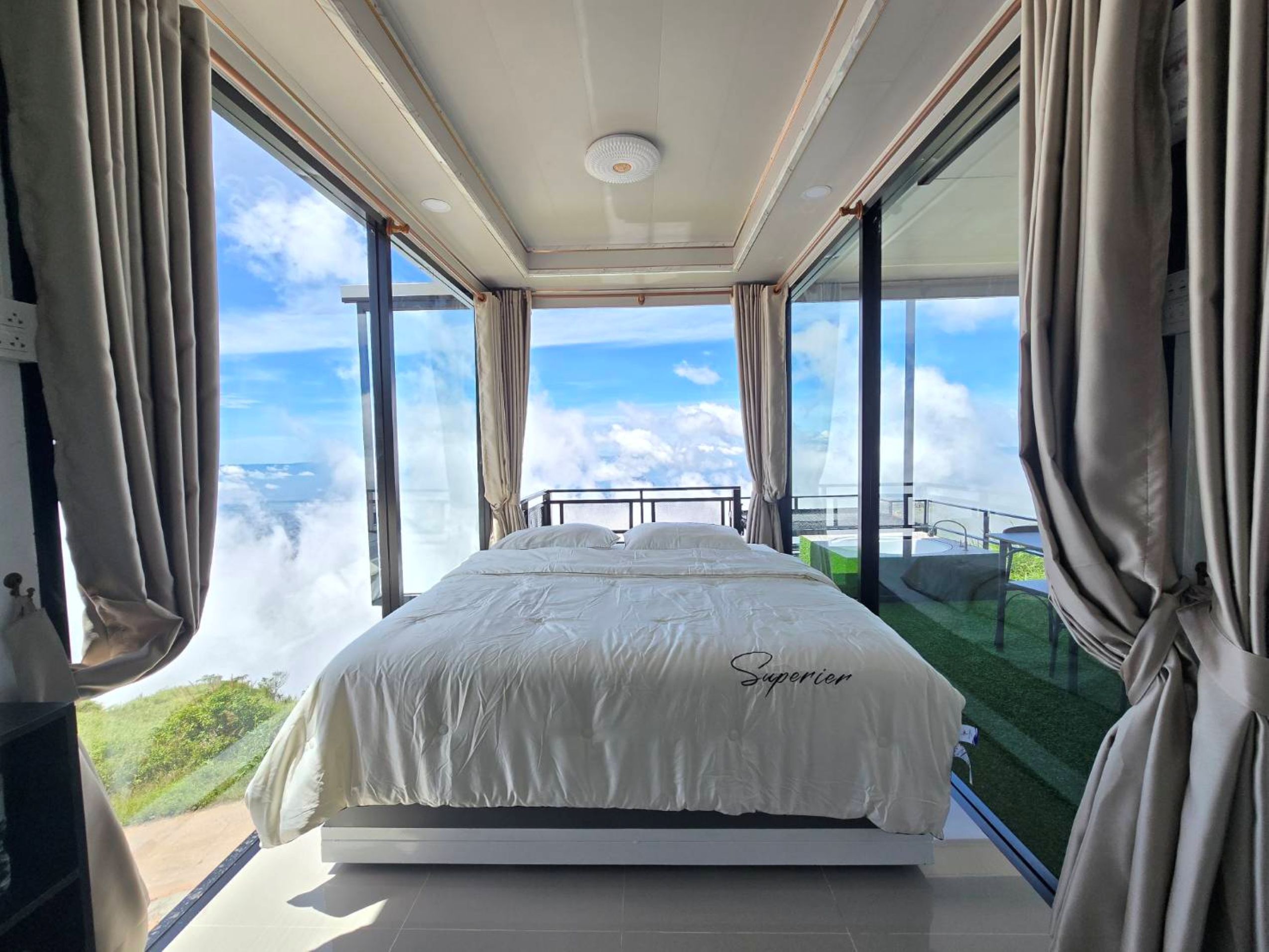 A bedroom with a large bed, a view of the sky, and a balcony with a glass railing.