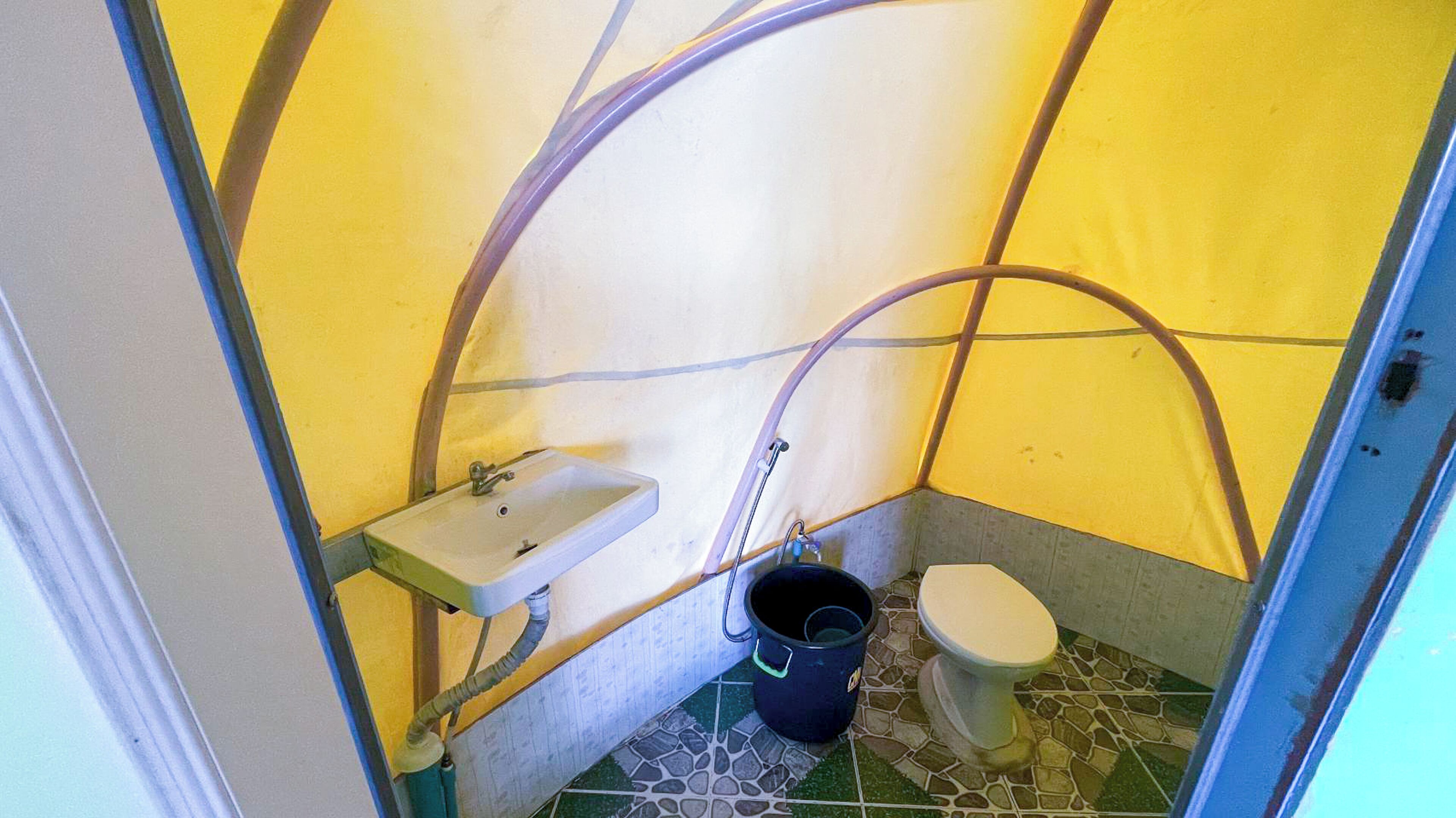 A small, enclosed bathroom with a sink, toilet, and a bucket.
