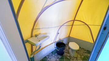 A small, enclosed bathroom with a sink, toilet, and a bucket.