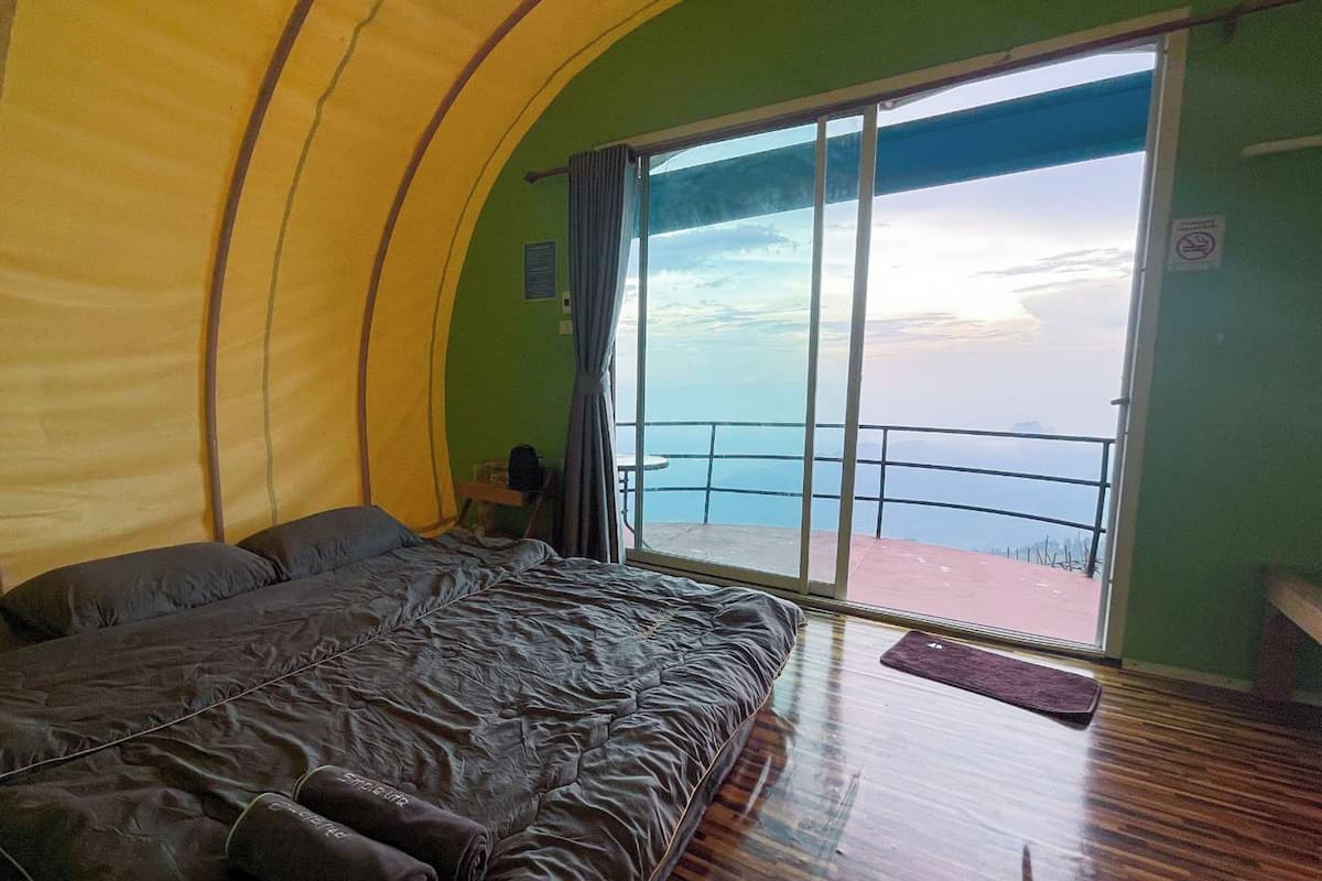 Una habitación con una cama grande, vista al mar a través de un ventanal corredero y una mesita con una silla.
