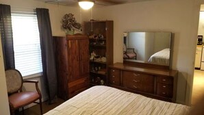 Une chambre à coucher comprenant un lit, une armoire en bois, une commode, une chaise et un grand miroir.