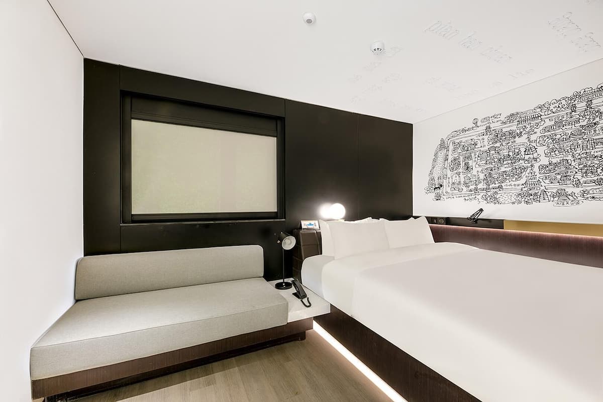 Habitació d'hotel moderna amb un llit gran, una zona d'estar, televisió penjada a la paret i un mural decoratiu.