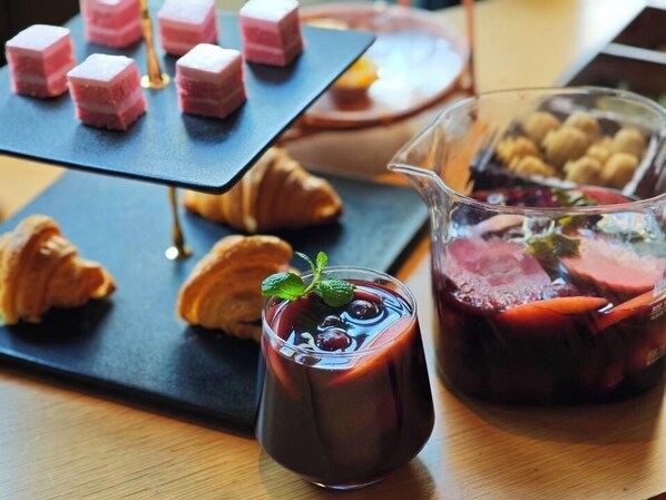 Una mesa de postres con cubos rosados, croissants y una jarra de bebida roja con menta.
