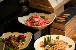 Una mesa de buffet con diversos platos, incluyendo verduras cortadas, carnes y pan.