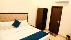 A bedroom with a tufted headboard, a bed with white bedding and a blue accent, a wardrobe, a door, and an air conditioning unit on the wall. - HOTEL INFRAVIEW (Dera Bassi)