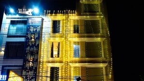 A hotel with multiple floors, illuminated by string lights, and two cars parked in front. - HOTEL INFRAVIEW (Dera Bassi)