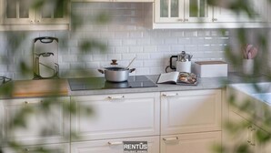 Una cocina con armarios blancos, una encimera con una olla, una tabla de cortar y un libro.