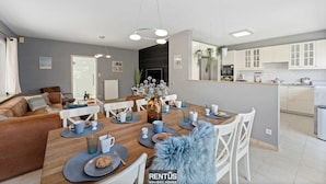 Una cocina moderna con armarios blancos, un comedor con mesa de madera y una sala de estar con sofá marrón.