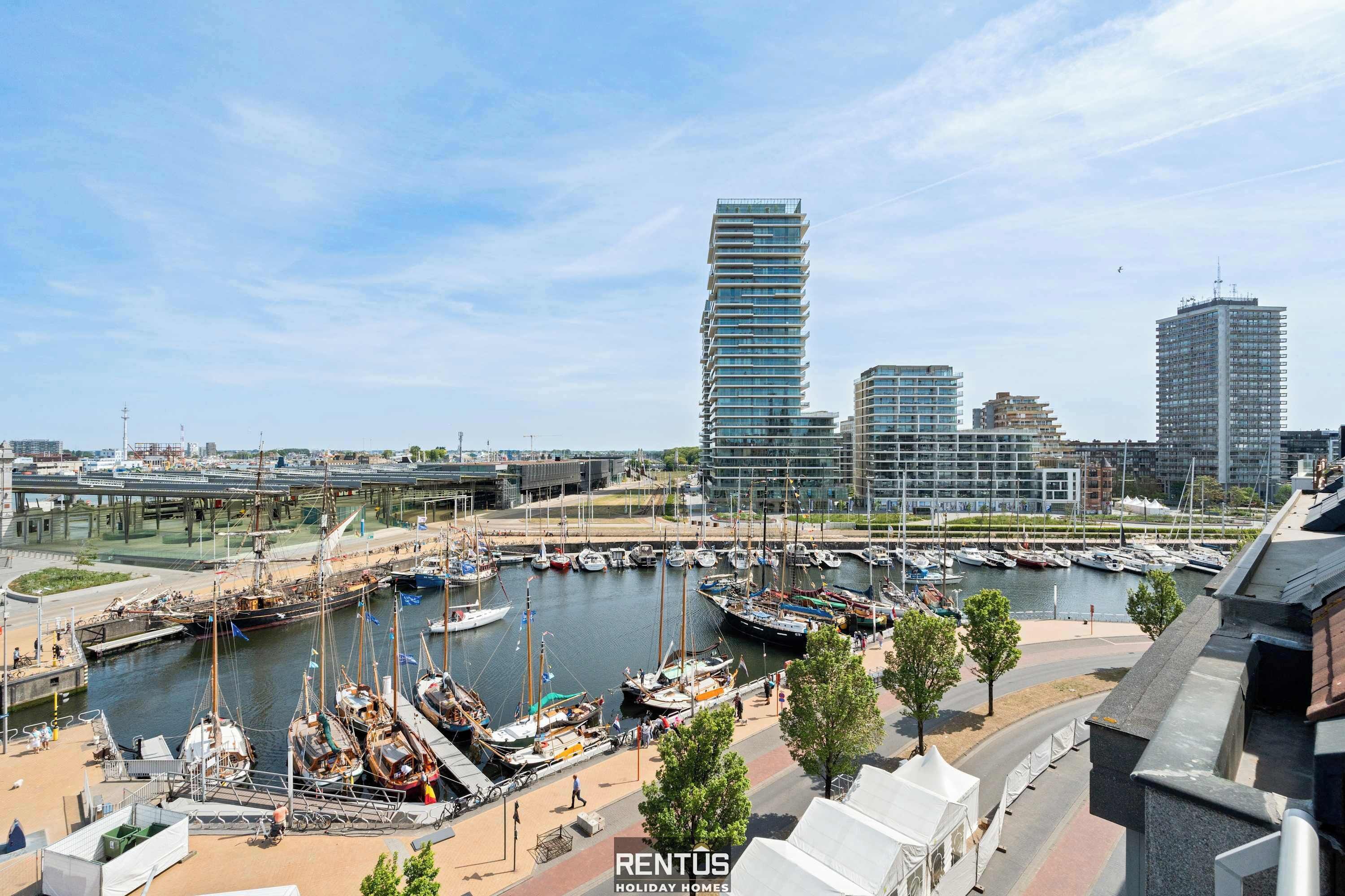 A marina with boats docked, a modern building with a unique design, and a bridge in the background.