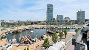 En småbåtshamn med förtöjda båtar, en modern byggnad med en unik design och en bro i bakgrunden.