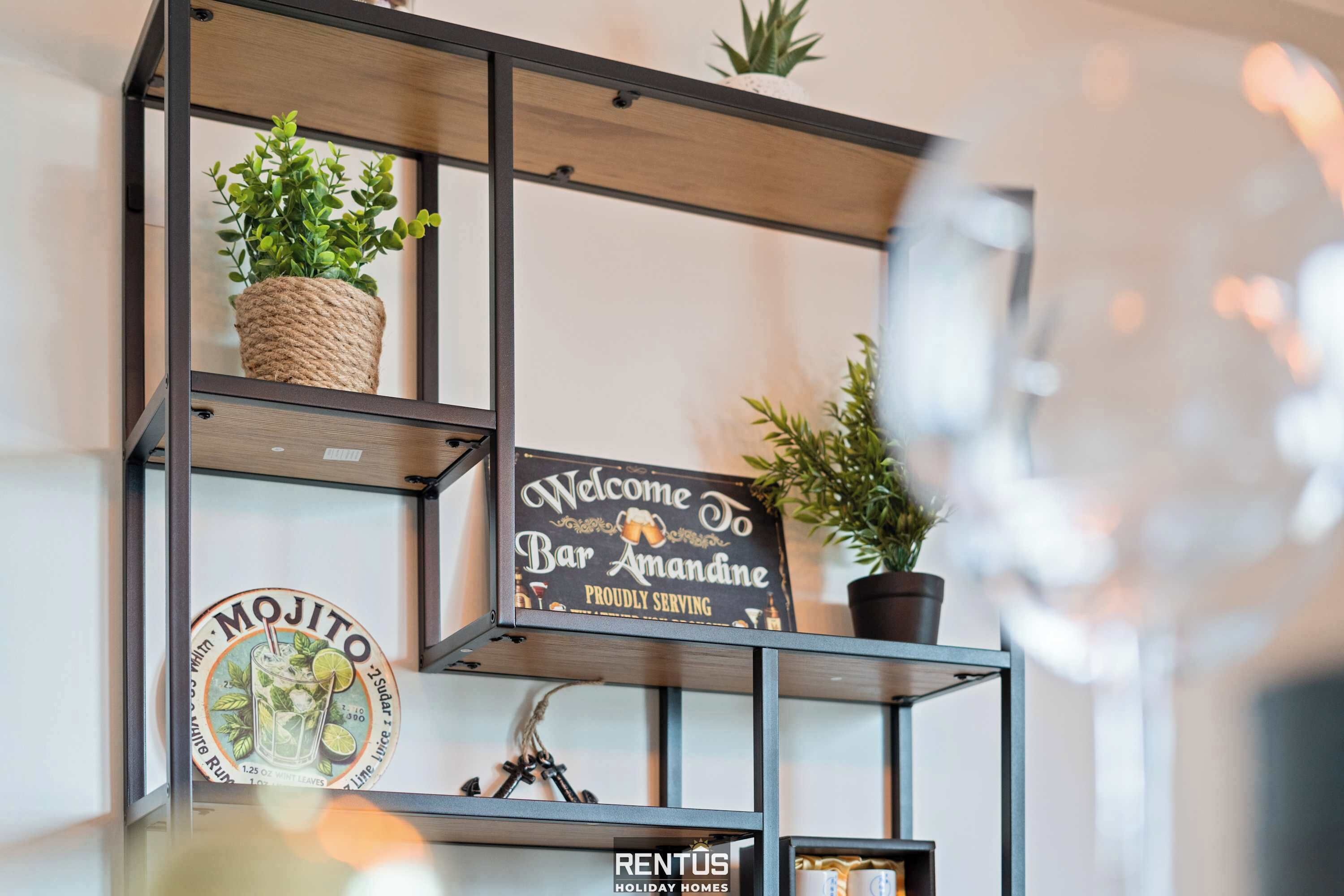Hyllyllä on kyltti, jossa lukee: ”Tervetuloa baariin Amandine”, ja Mojito-lasinalusta.