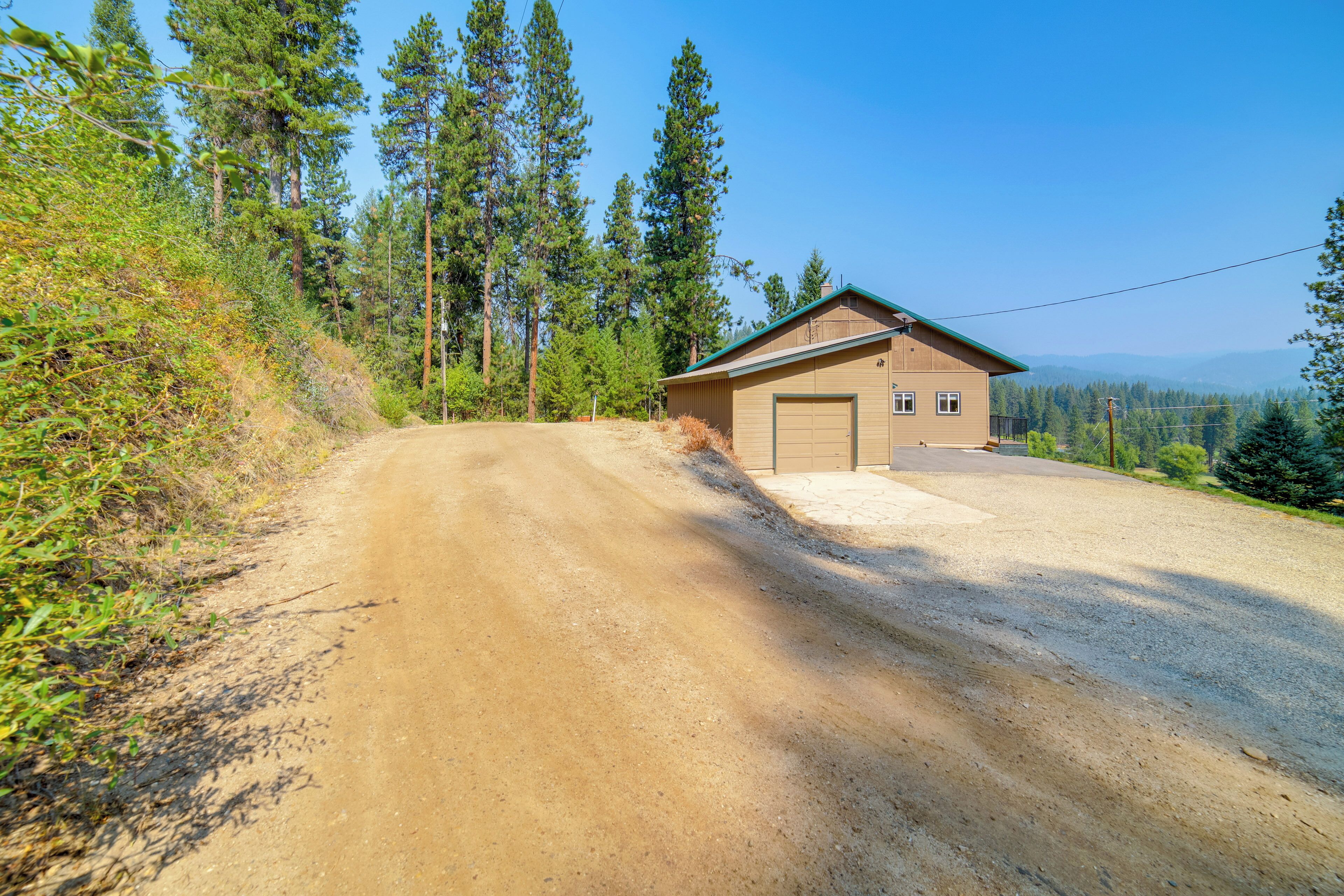 Un bâtiment à deux étages avec un garage, entouré d’un chemin de terre et d’une forêt dense.