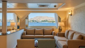 Un interior lujoso con un conjunto de sofás, una mesa y vistas a un cuerpo de agua y una montaña.