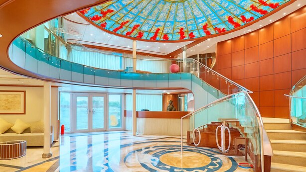 Un amplio atrio con una escalera de cristal, una fuente central y vistas al agua.