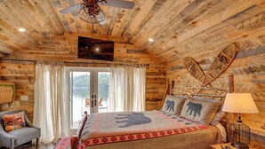 Un dormitorio de cabaña de madera con una cama, una silla, una mesita de noche y vistas al exterior.