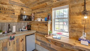 Una cocina de estilo rústico tipo cabaña, con paredes de madera, un ventanal y varios electrodomésticos de cocina.
