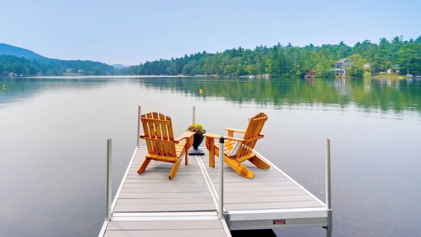 Un muelle de madera con dos sillas y una mesa, con vista a un lago tranquilo bordeado por un bosque.